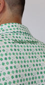 Close-up of a person wearing a white golf polo with green four-leaf clover pattern and 'Mulligan Hooligan' printed vertically in green script.