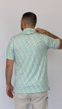 A man viewed from behind wearing a short-sleeve button-up shirt with a green and white clover pattern, paired with light beige pants, against a plain light gray background.