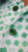 Close-up of a white button-up shirt with a green shamrock and clover pattern, featuring a green button with 'Mulligan Hooligan' text.