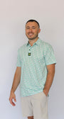A man wearing a light green and white Clover patterned short-sleeve polo shirt with beige shorts, standing against a plain white background.