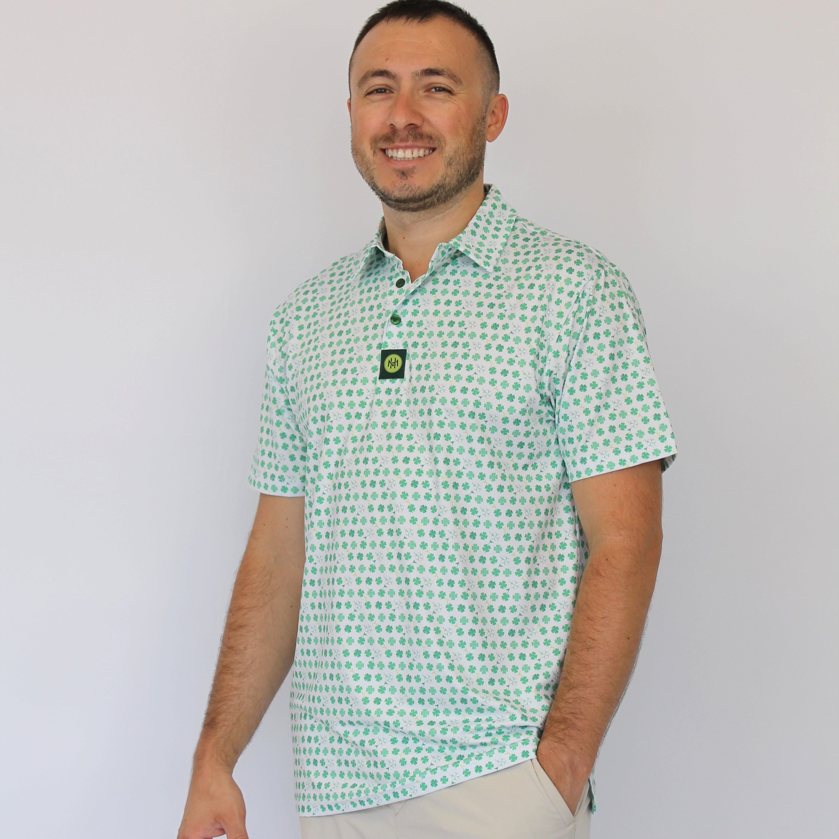 A man wearing a light green and white Clover patterned short-sleeve polo shirt with beige shorts, standing against a plain white background.