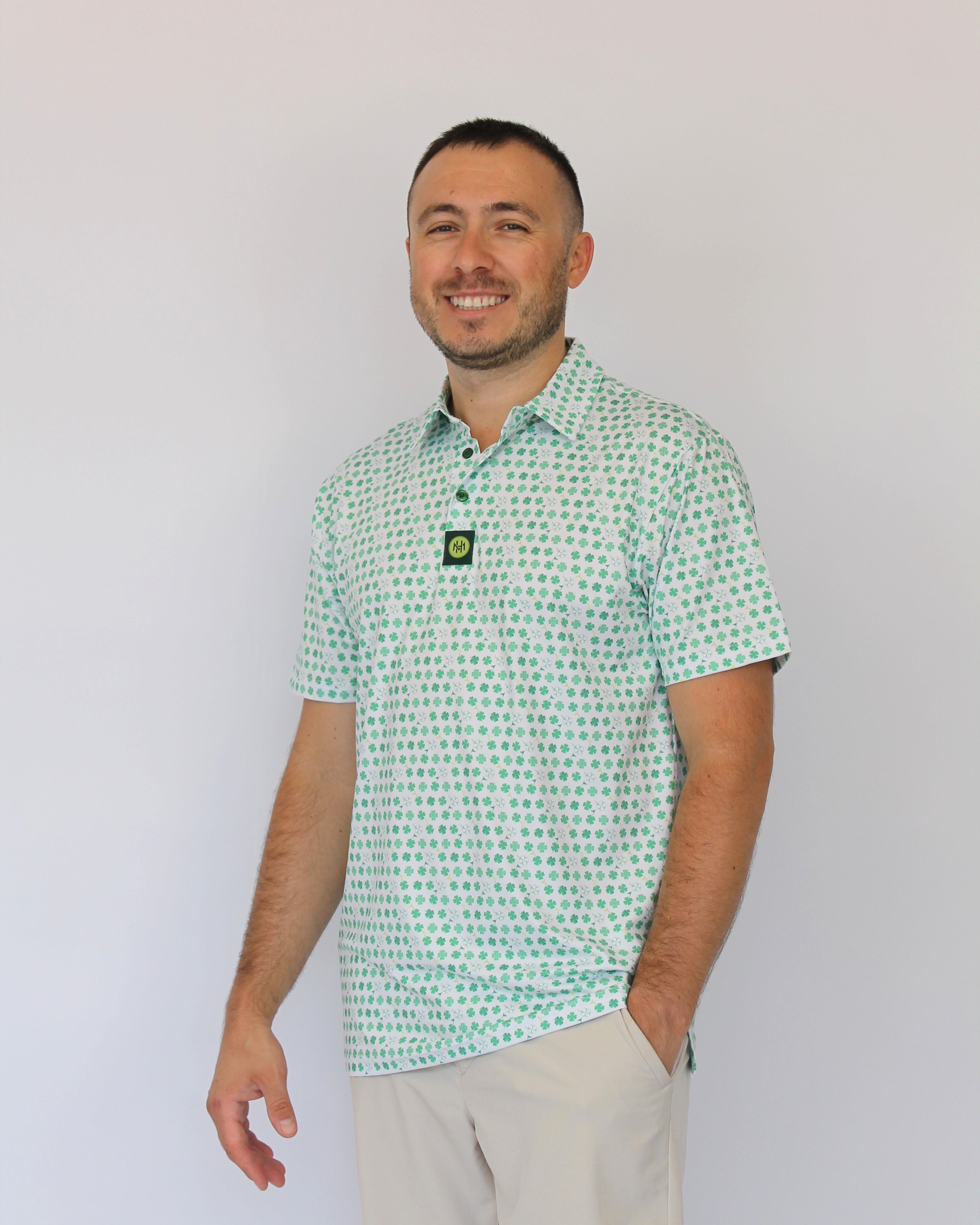 A man wearing a light green and white Clover patterned short-sleeve polo shirt with beige shorts, standing against a plain white background.
