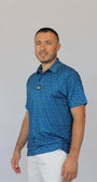A man wearing the Amen Clover Golf Polo blue short-sleeve polo shirt with a small yellow clover pattern and white pants, shown against a plain light gray background.