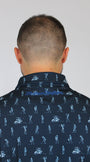 Back view of a man wearing a dark navy blue collared shirt with a light blue golfing skeletons golf-themed all-over print, featuring golfers and carts. The brand name 'Mulligan Hooligan' is visible in script on the inner neck label.