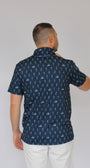 A man wearing a navy blue short-sleeve button-up shirt with a repeating white golfing skeletons pattern, paired with white pants, shown from a side profile against a plain light gray background.