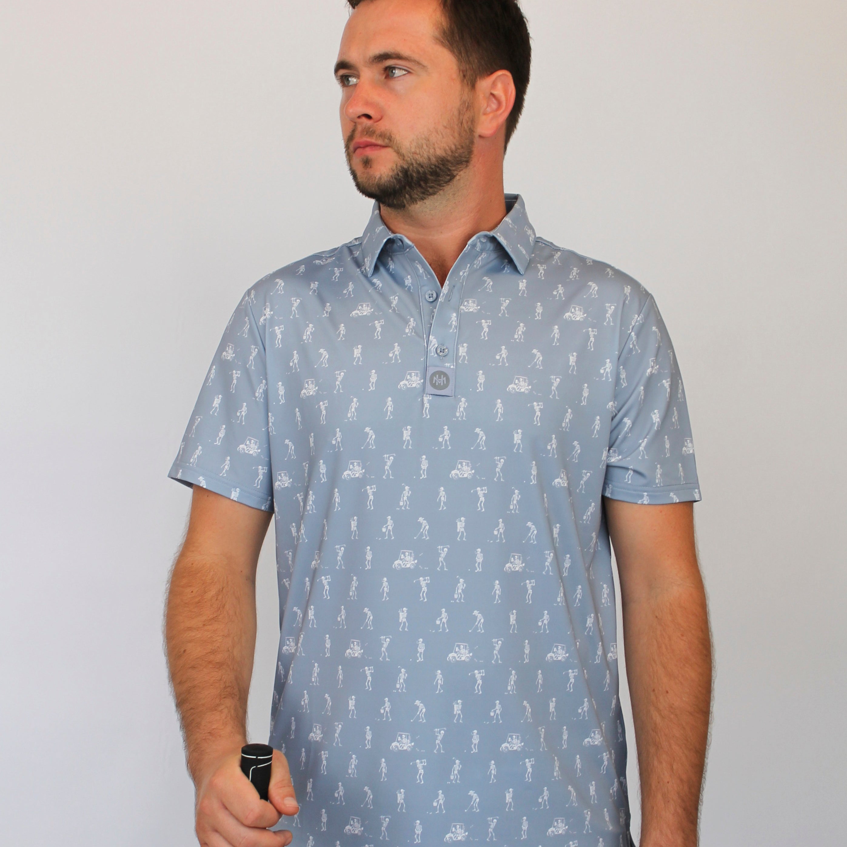 A man wearing a light gray short-sleeve polo shirt with white goofing skeletons pattern, standing against a plain light gray background.