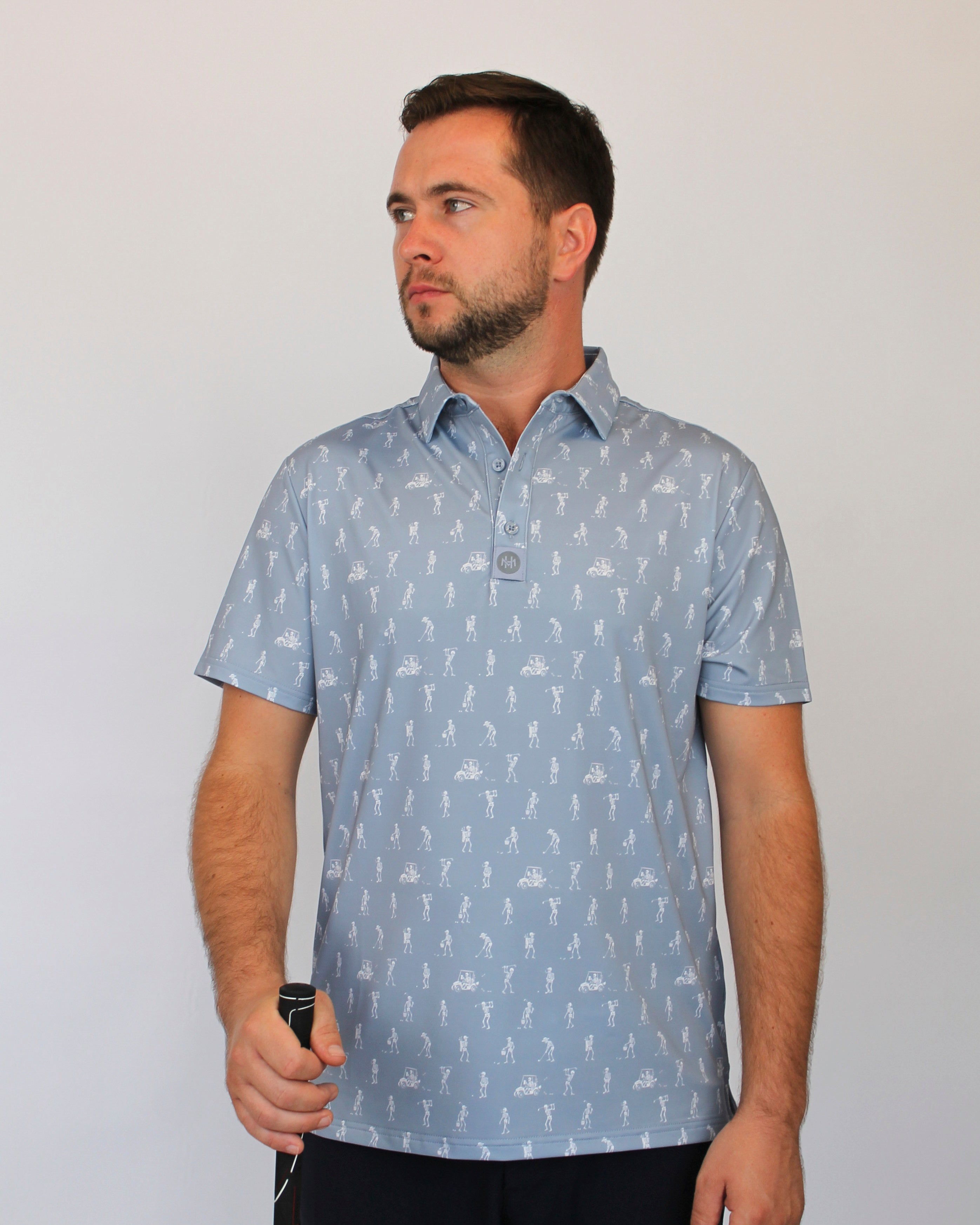 A man wearing a light gray short-sleeve polo shirt with white goofing skeletons pattern, standing against a plain light gray background.