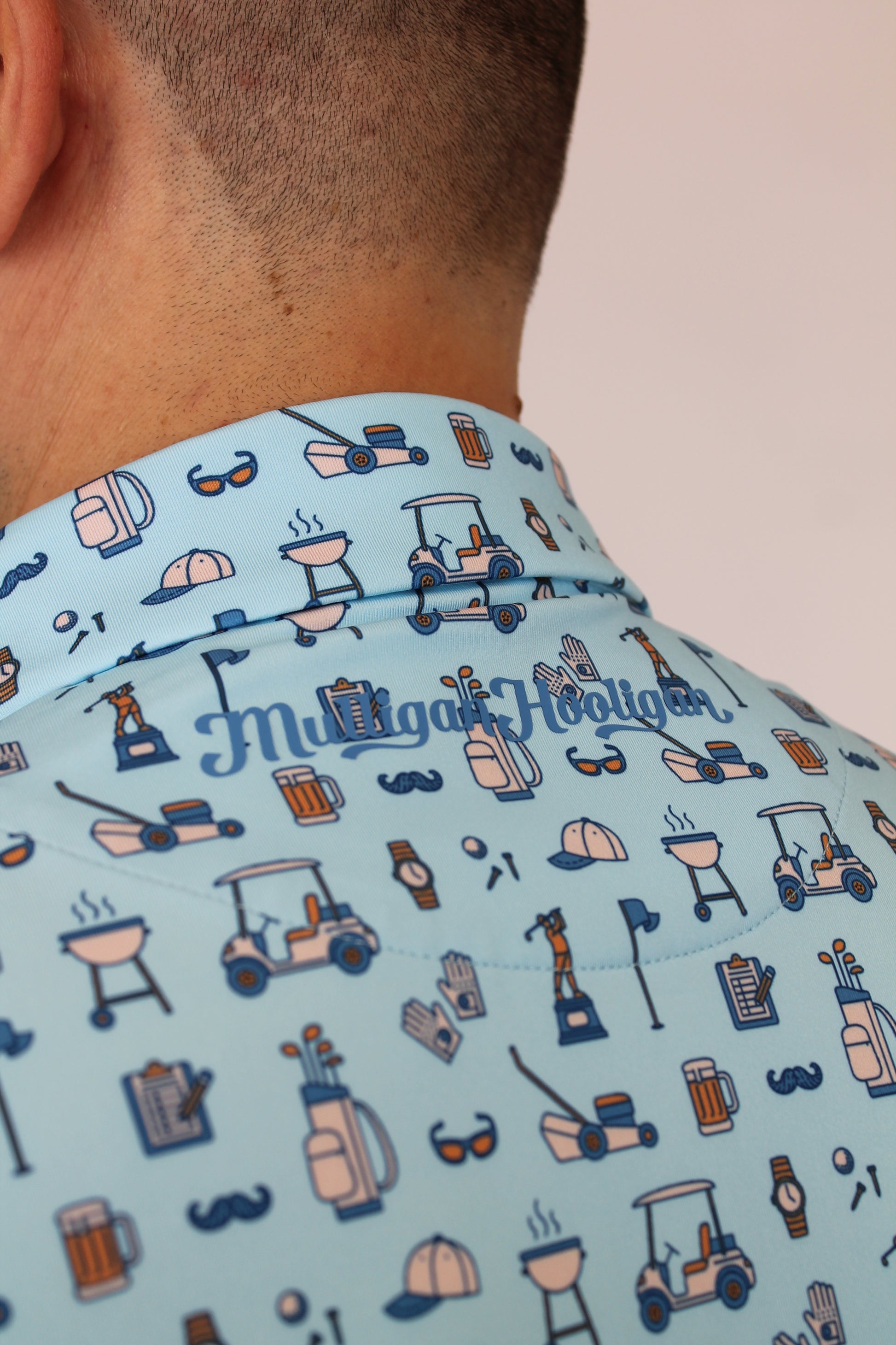 Close-up of a person wearing a light blue Best Dad By Par short-sleeve shirt with a golf-themed all-over print and vertical 'Mulligan Hooligan' text on the collar.