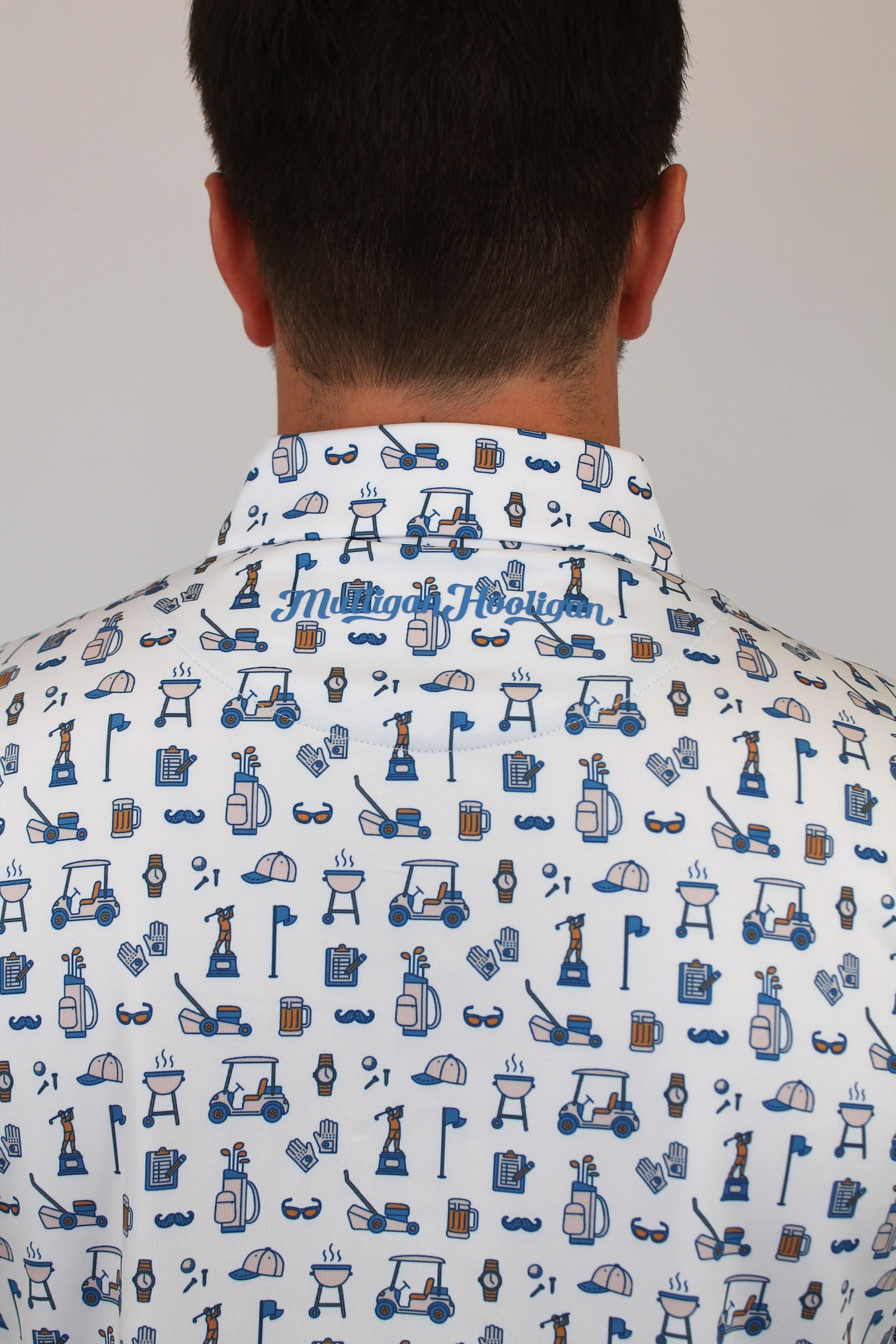 Back view of a man wearing a white button-down shirt with  blue Dad golf-themed pattern, featuring golf carts, clubs, flags, and a cursive 'Mulligan Hooligan' script on the collar.