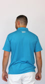 A man viewed from behind wearing a bright turquoise blue short-sleeve polo shirt and white pants, standing against a plain light gray background.