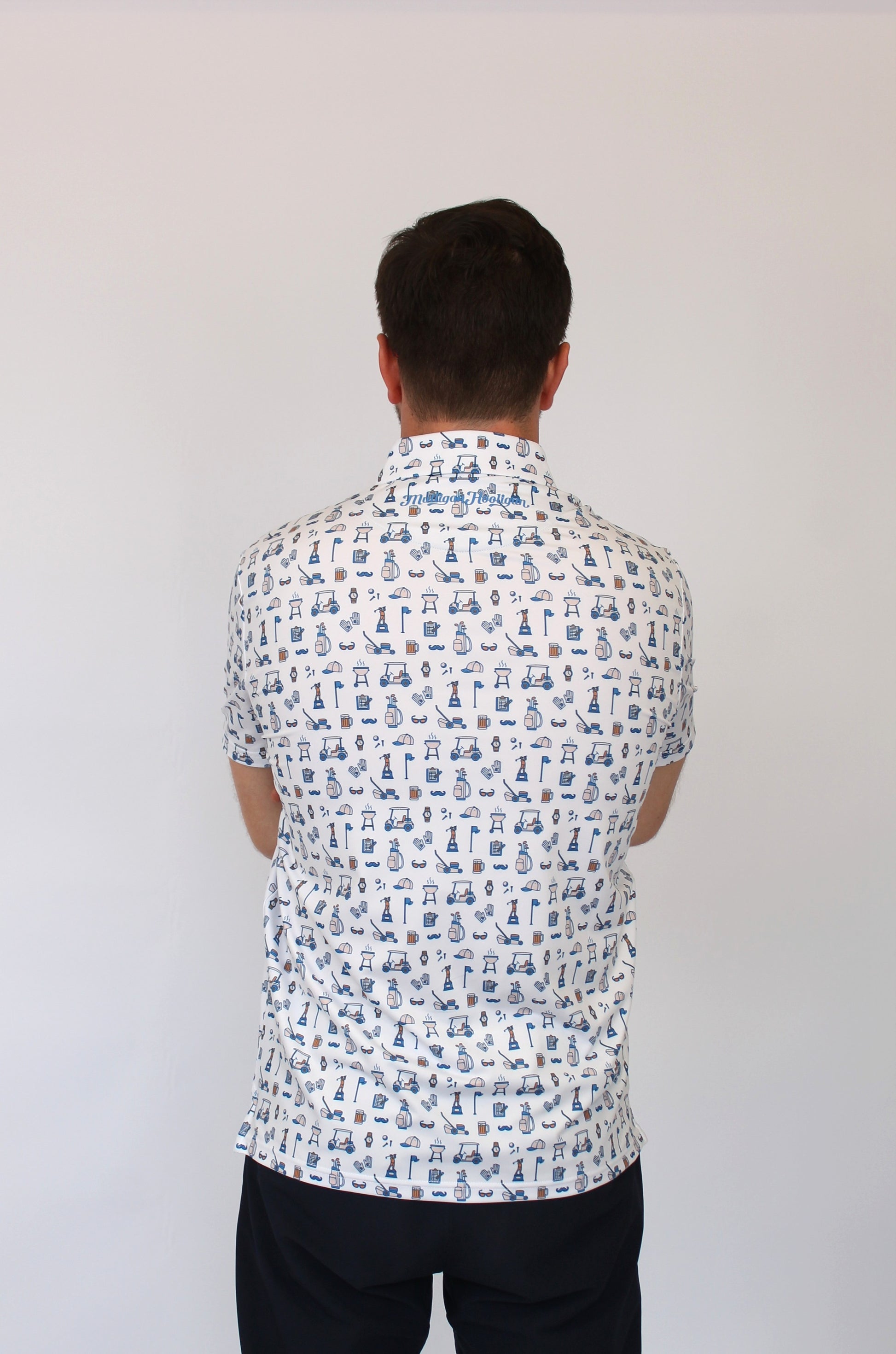 A man viewed from behind wearing a white short-sleeve button-up shirt with a blue golf Dad-themed all-over print, paired with black pants, against a plain light gray background.