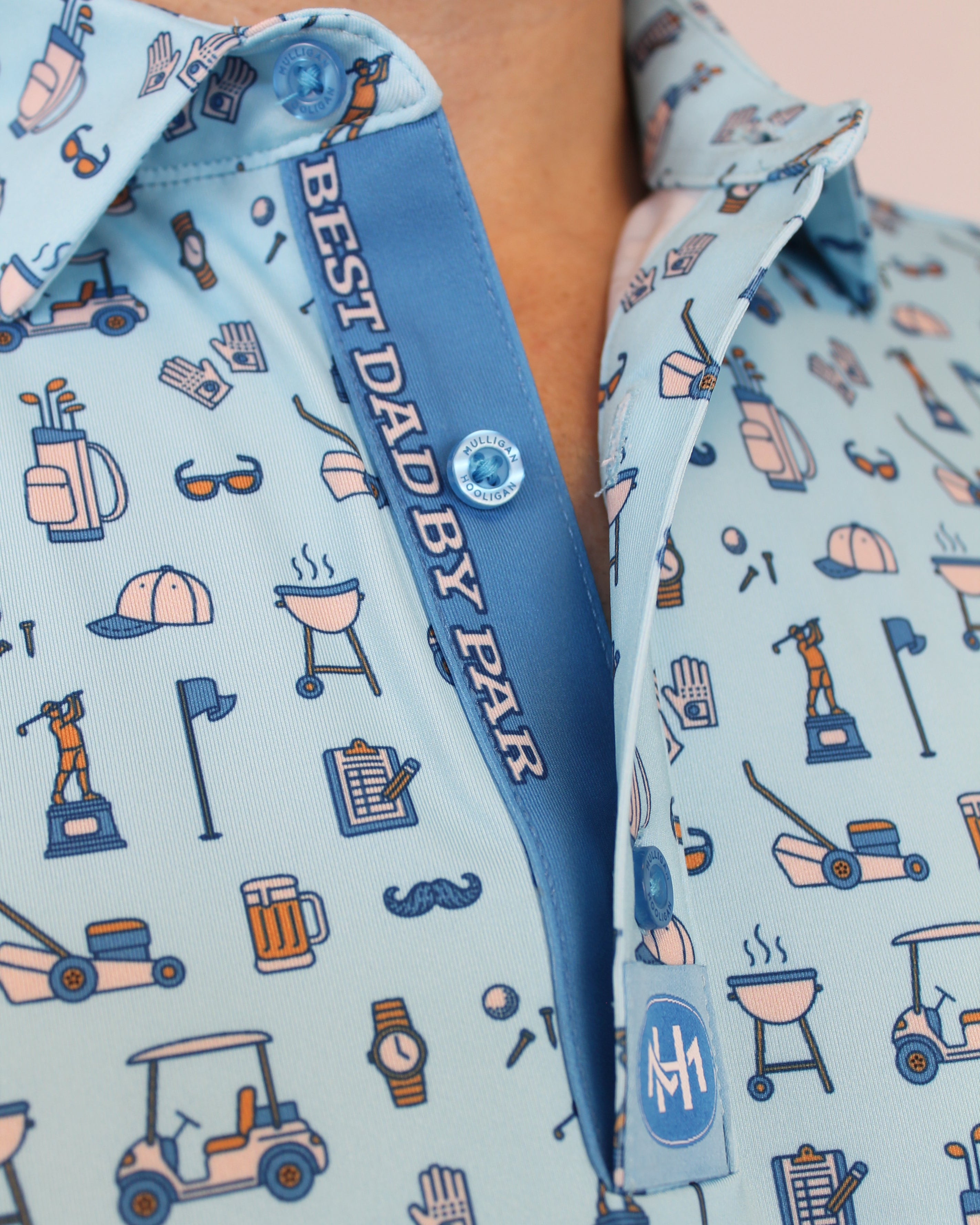 Close-up of a light blue patterned button-up shirt with a blue placket reading 'BEST DAD BY PAR' and a small circular logo patch.