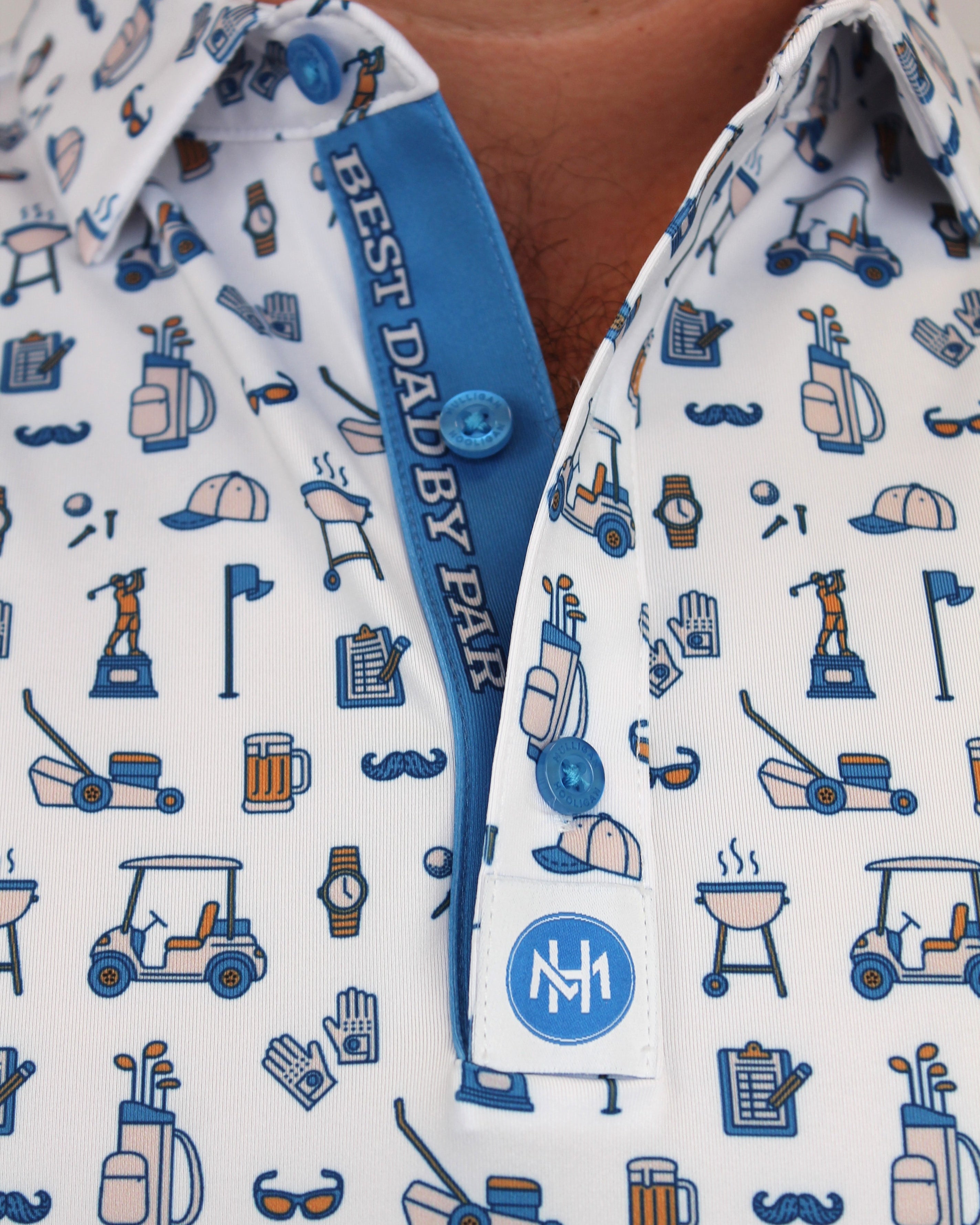 Close-up of a man wearing a white button-down shirt with a blue and navy Dad golf-themed print, featuring a collar, and a custom planchet saying ''Best Dad By Par'' blue placket, and a white chest patch with a circular 'NM' logo.