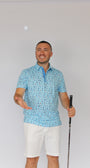 A man wearing a light blue patterned Best Dad By Par short-sleeve polo shirt and white shorts, holding a golf club and smiling against a plain white background.