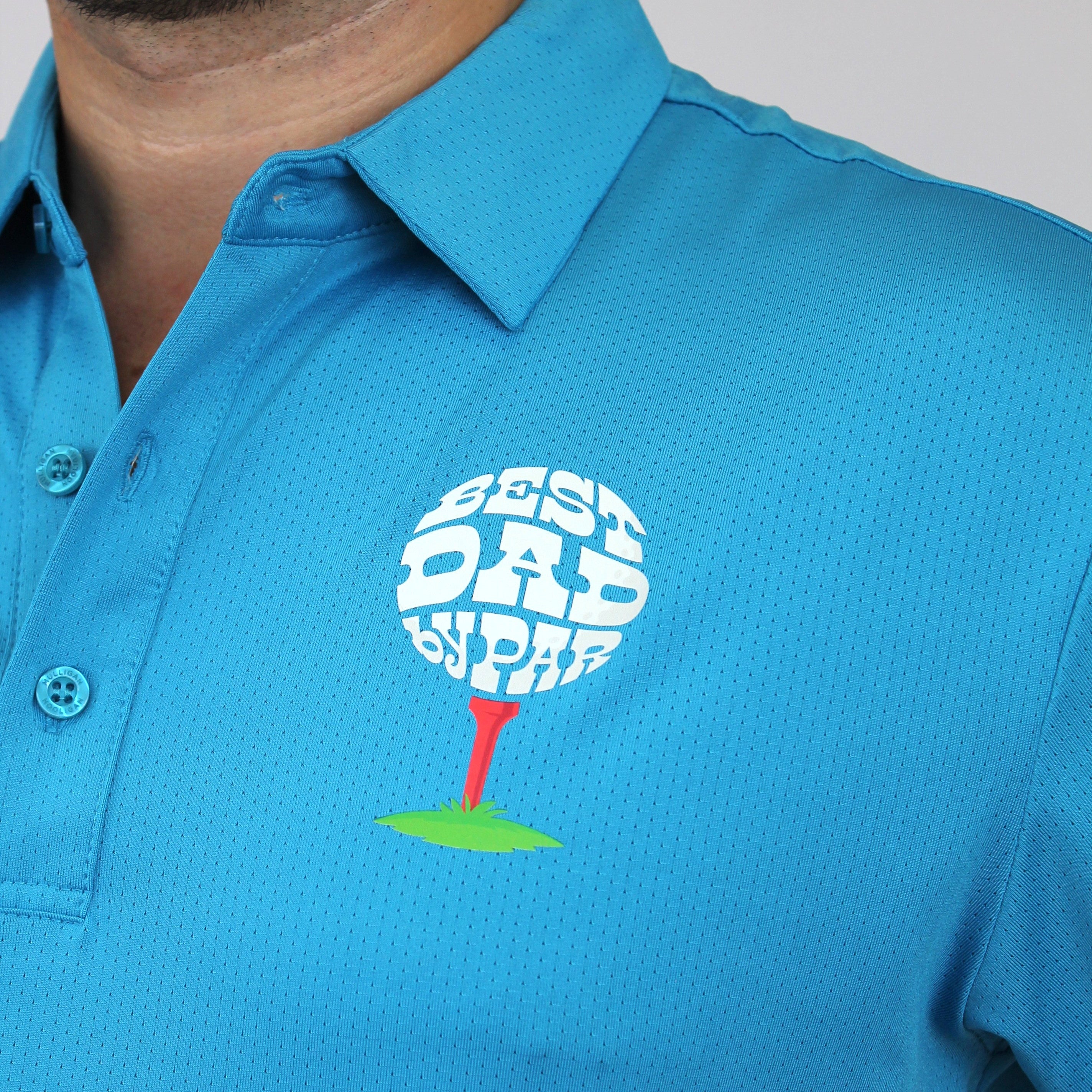 A close-up of a man wearing a bright blue polo shirt with a custom golf-themed chest graphic. The graphic features a white golf ball with the words 'BEST DAD BY PAR' in white, resting on a red tee over a green patch of grass.