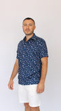 A man wearing a navy blue Best Dad By Par short-sleeve button-up shirt with a white golf dad pattern, paired with white shorts, standing against a plain white background.