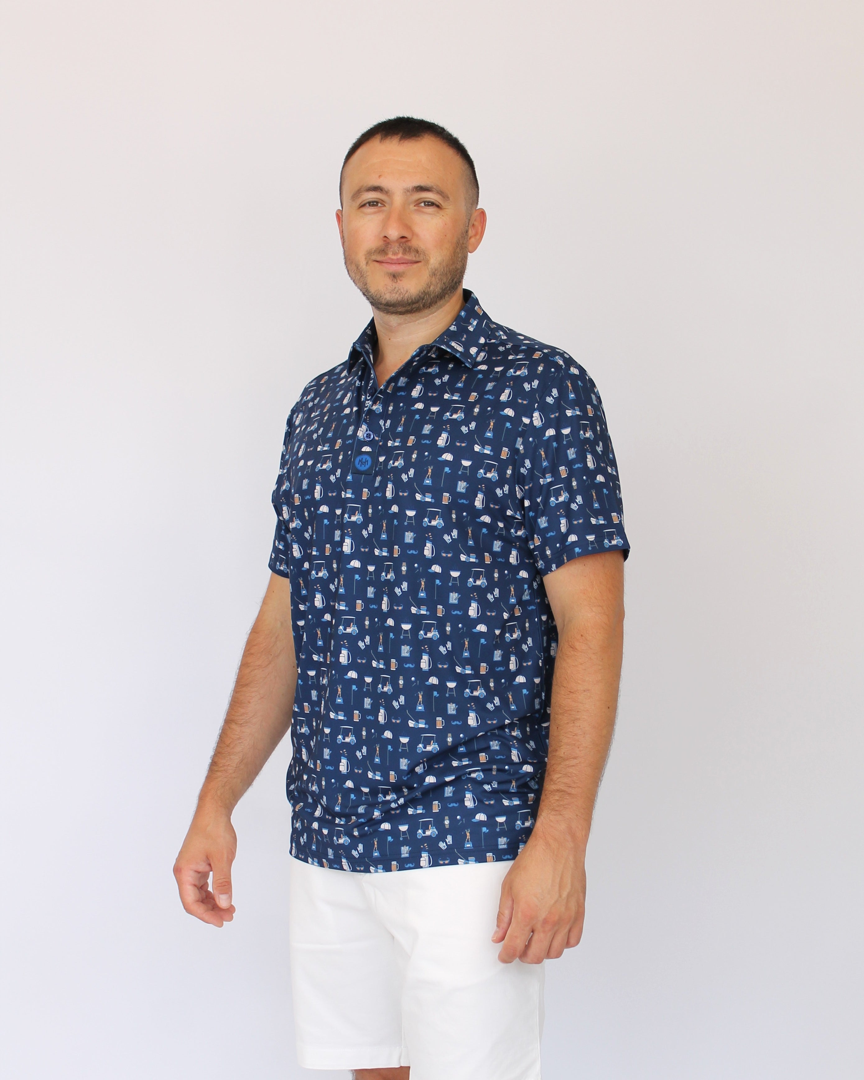A man wearing a navy blue Best Dad By Par short-sleeve button-up shirt with a white golf dad pattern, paired with white shorts, standing against a plain white background.