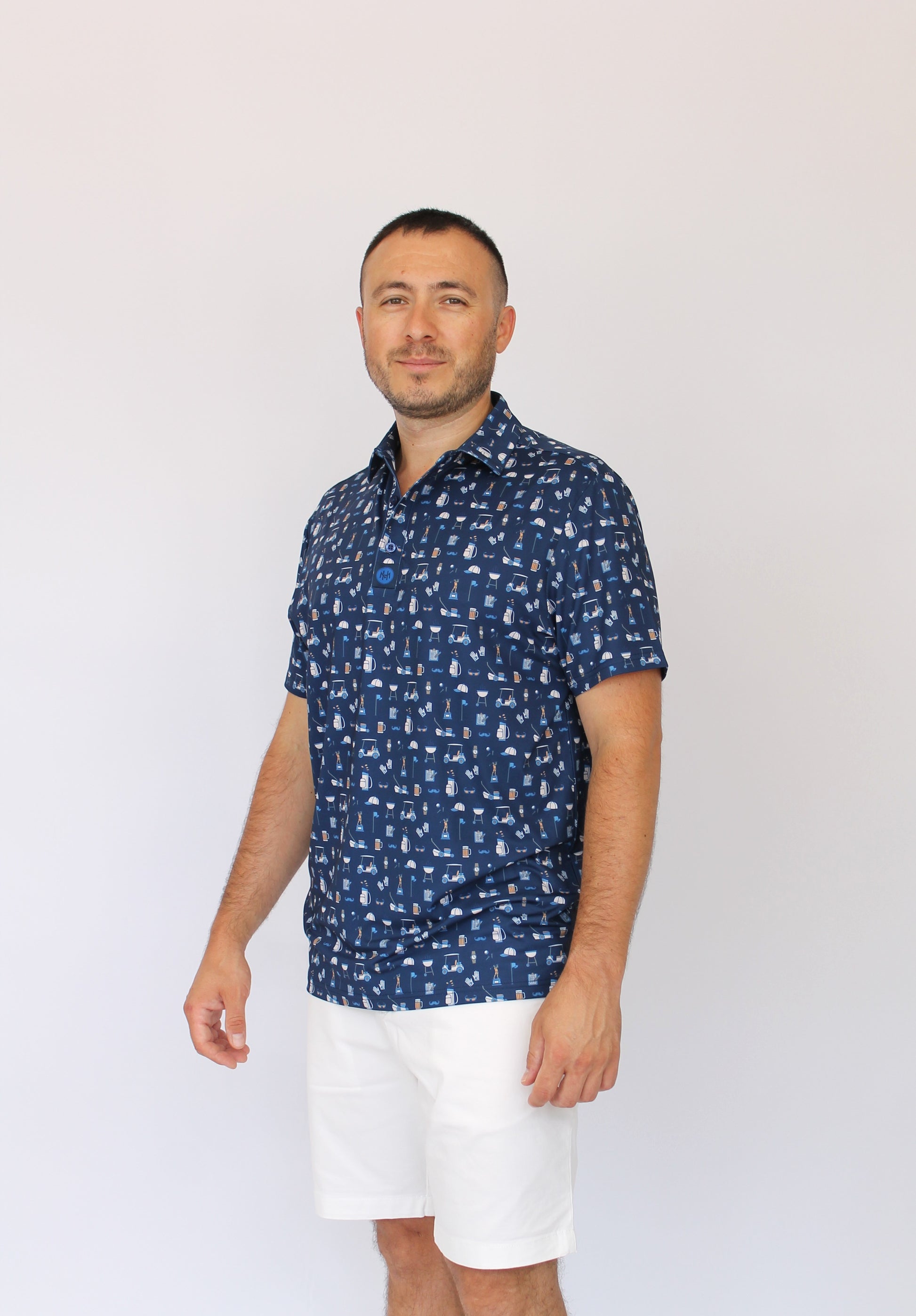 A man wearing a navy blue Best Dad By Par short-sleeve button-up shirt with a white golf dad pattern, paired with white shorts, standing against a plain white background.
