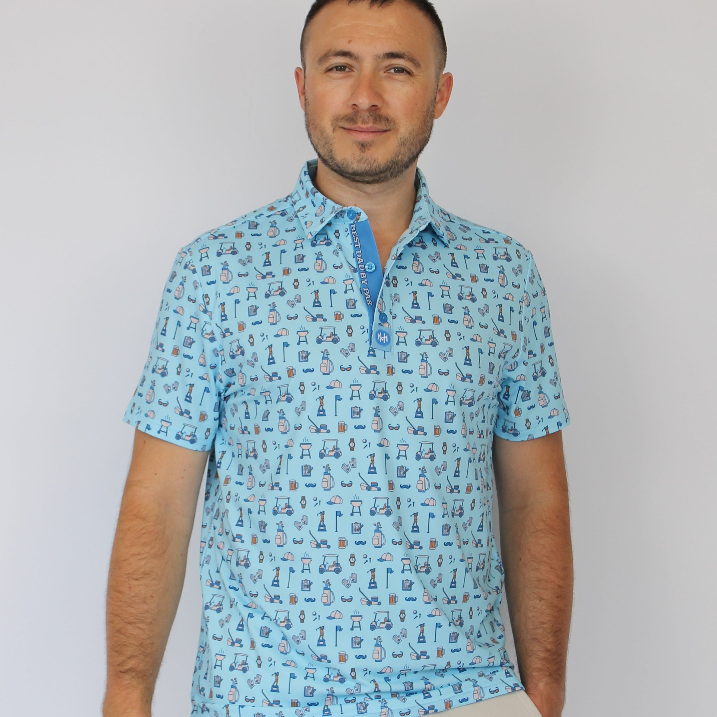 A man wearing a light blue short-sleeve polo shirt with Golf dad repeating blue pattern, paired with light beige trousers, photographed against a plain white background.