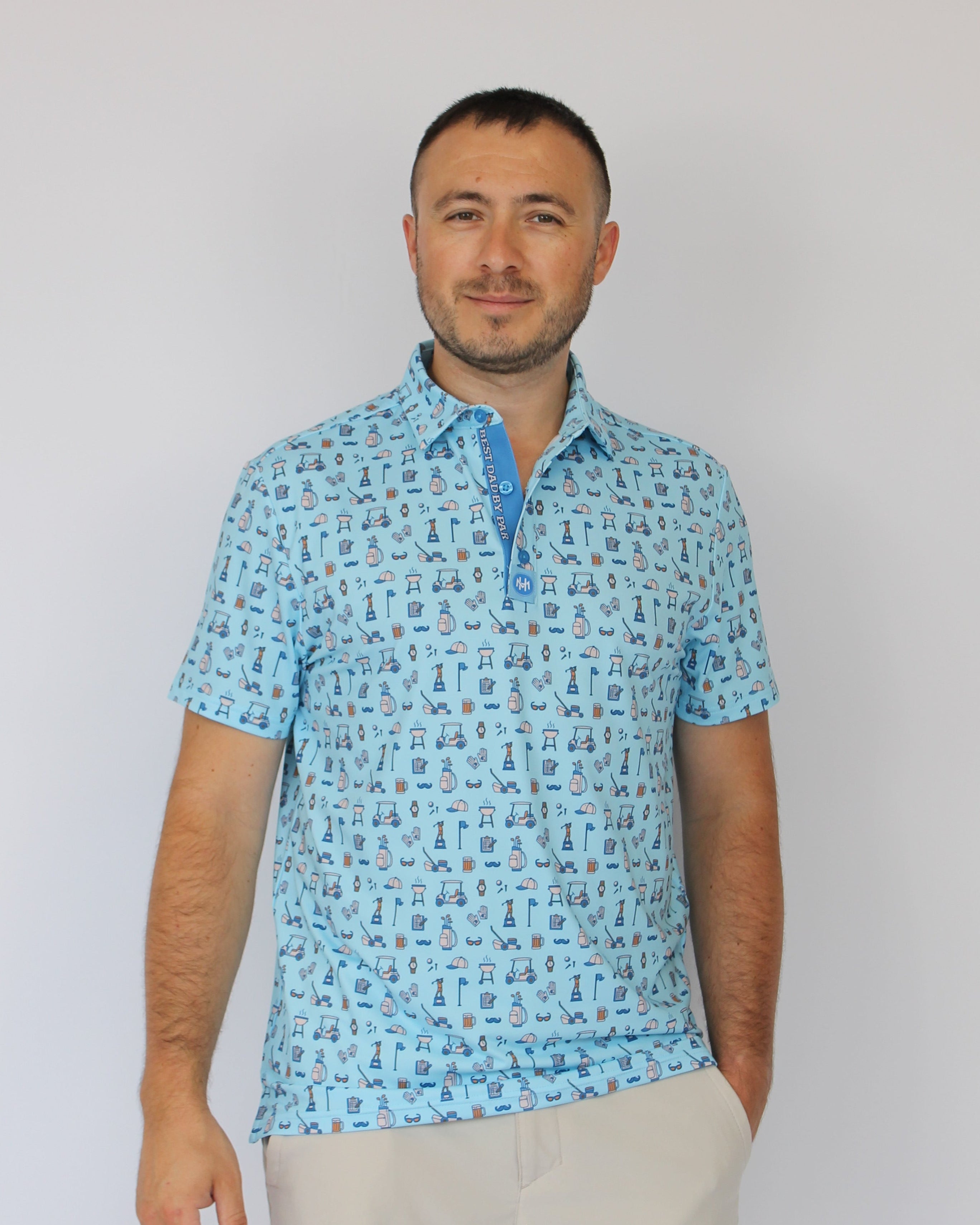 A man wearing a light blue short-sleeve polo shirt with Golf dad repeating blue pattern, paired with light beige trousers, photographed against a plain white background.