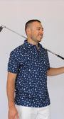 A man wearing a navy blue short-sleeve polo shirt with a white and light blue golf dad-themed pattern, holding a golf club over his shoulder against a plain light background.