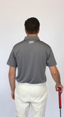 A man viewed from behind wearing a gray short-sleeve polo shirt and off-white shorts, holding a golf club with a red grip against a plain light background.