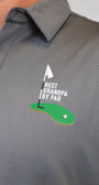 Close-up of a gray perforated polo shirt worn by a person, featuring a golf-themed chest graphic with a green putting green, white flag, and the text 'BEST GRANDPA BY PAR'.