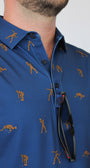 A close-up of a man wearing a blue short-sleeve button-up shirt with Bigfoot golf-themed print of golfers and a golf ball, with black sunglasses hanging from the collar.