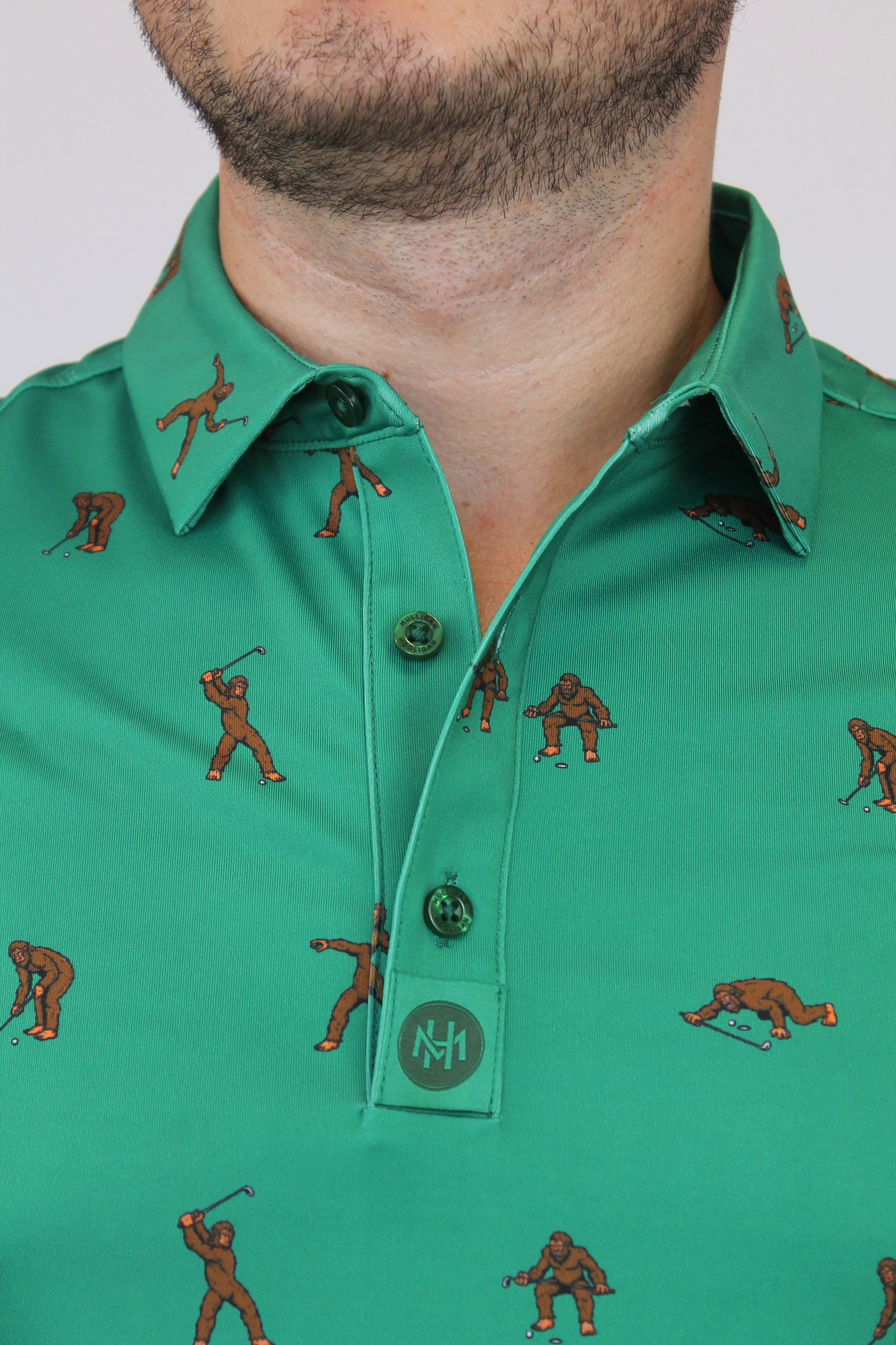 Close-up of a man wearing a green Bigfoot Patterned short-sleeve button-up shirt with a brown figure print and a chest pocket.