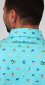 A man shown from the back wearing a light blue collared shirt with a colorful golf-themed and beach-theme print of tees, greens, holes, and golf carts. The brand name 'Mulligan Hooligan' is printed in script across the collar.