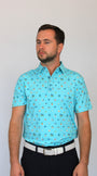 A man wearing a light blue short-sleeve polo shirt with a small Coastal Links, Myrtle Beach, SC, all-over pattern, paired with black trousers and a white belt, standing against a plain light gray background.