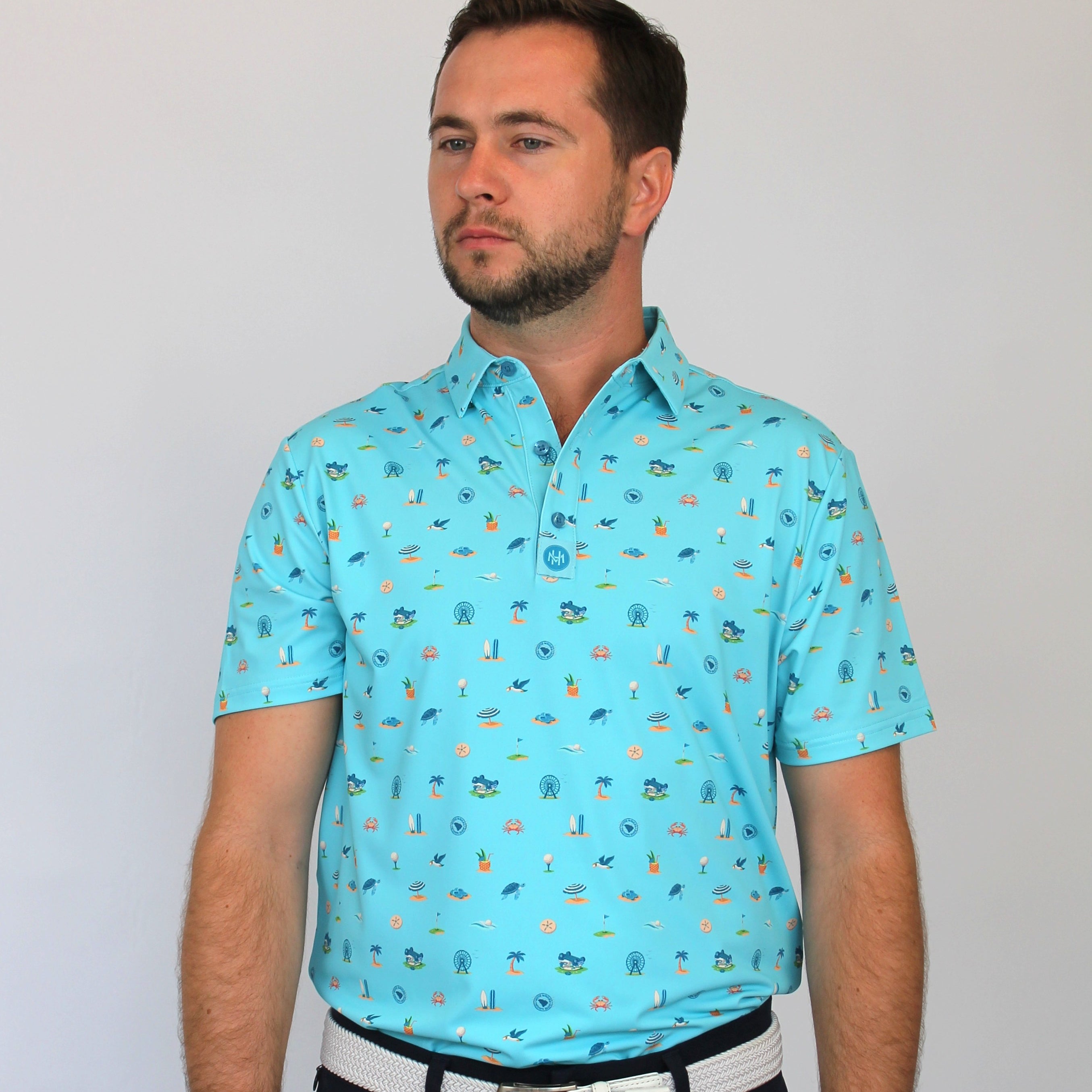 A man wearing a light blue short-sleeve polo shirt with a small Coastal Links, Myrtle Beach, SC, all-over pattern, paired with black trousers and a white belt, standing against a plain light gray background.