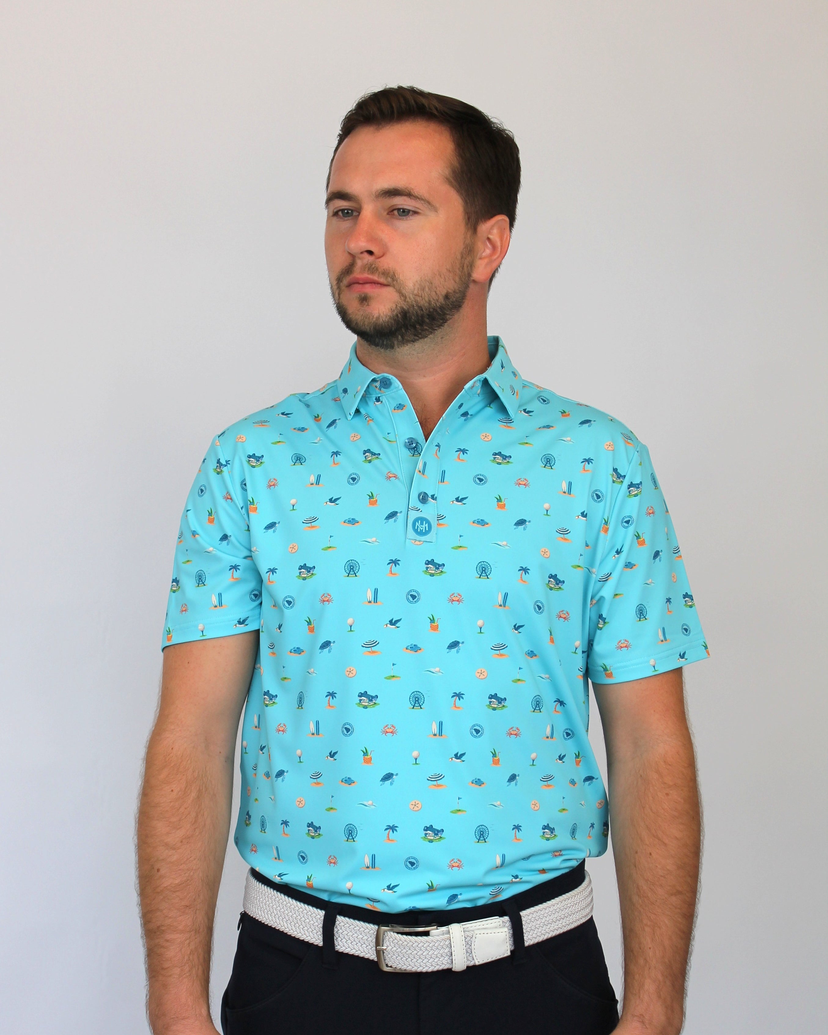 A man wearing a light blue short-sleeve polo shirt with a small Coastal Links, Myrtle Beach, SC, all-over pattern, paired with black trousers and a white belt, standing against a plain light gray background.
