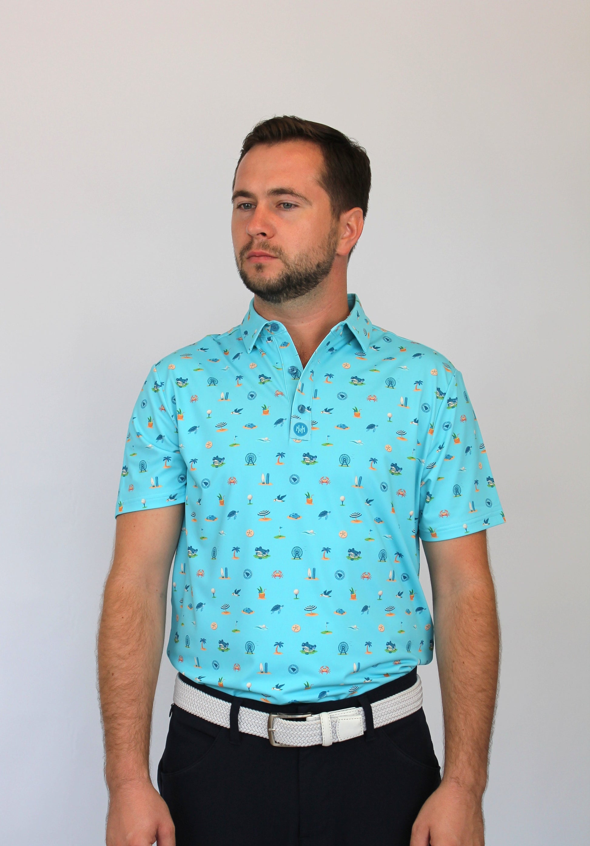 A man wearing a light blue short-sleeve polo shirt with a small Coastal Links, Myrtle Beach, SC, all-over pattern, paired with black trousers and a white belt, standing against a plain light gray background.