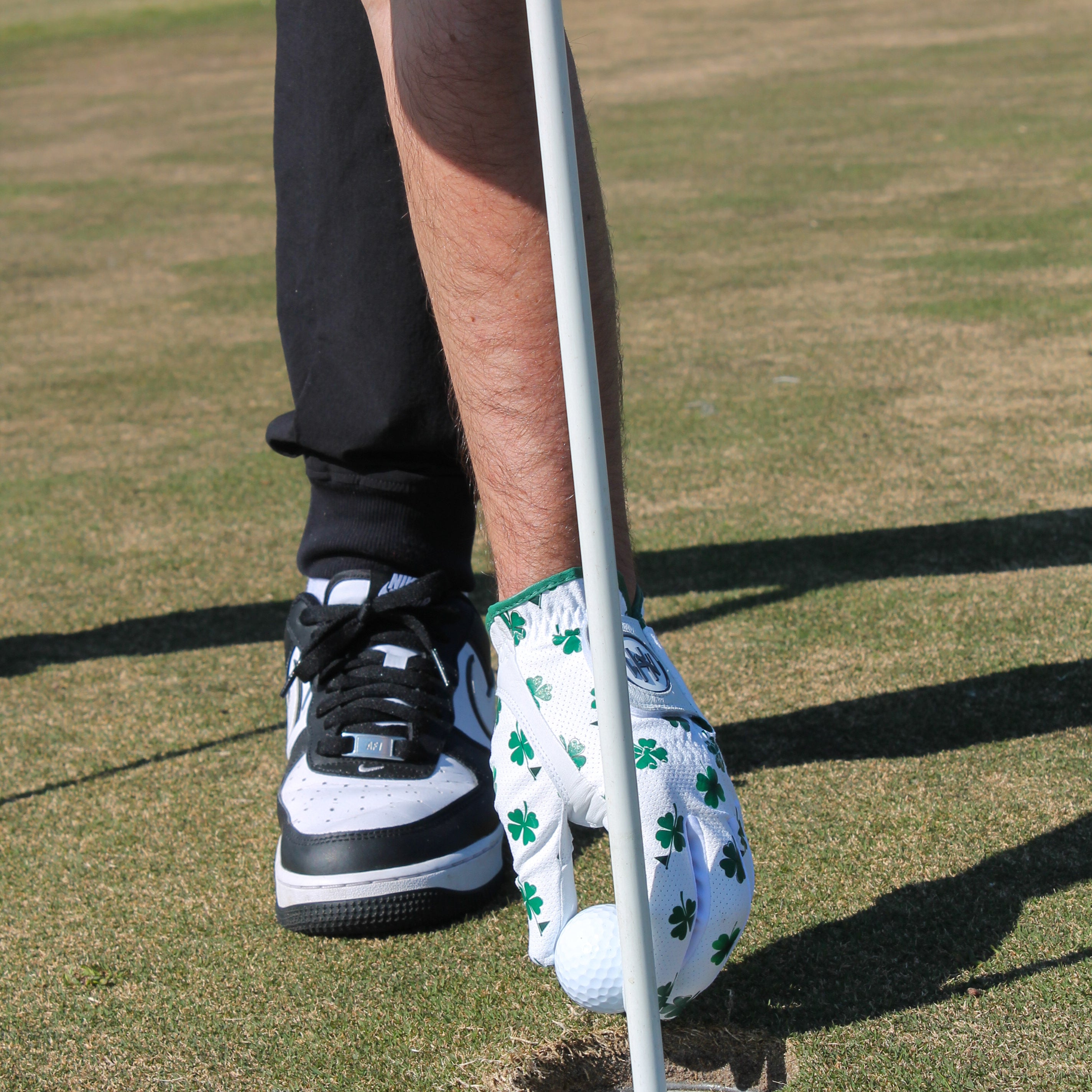 Person preparing to putt and he is removing the golf ball from the hole in a premium 'Clover Luck' golf glove