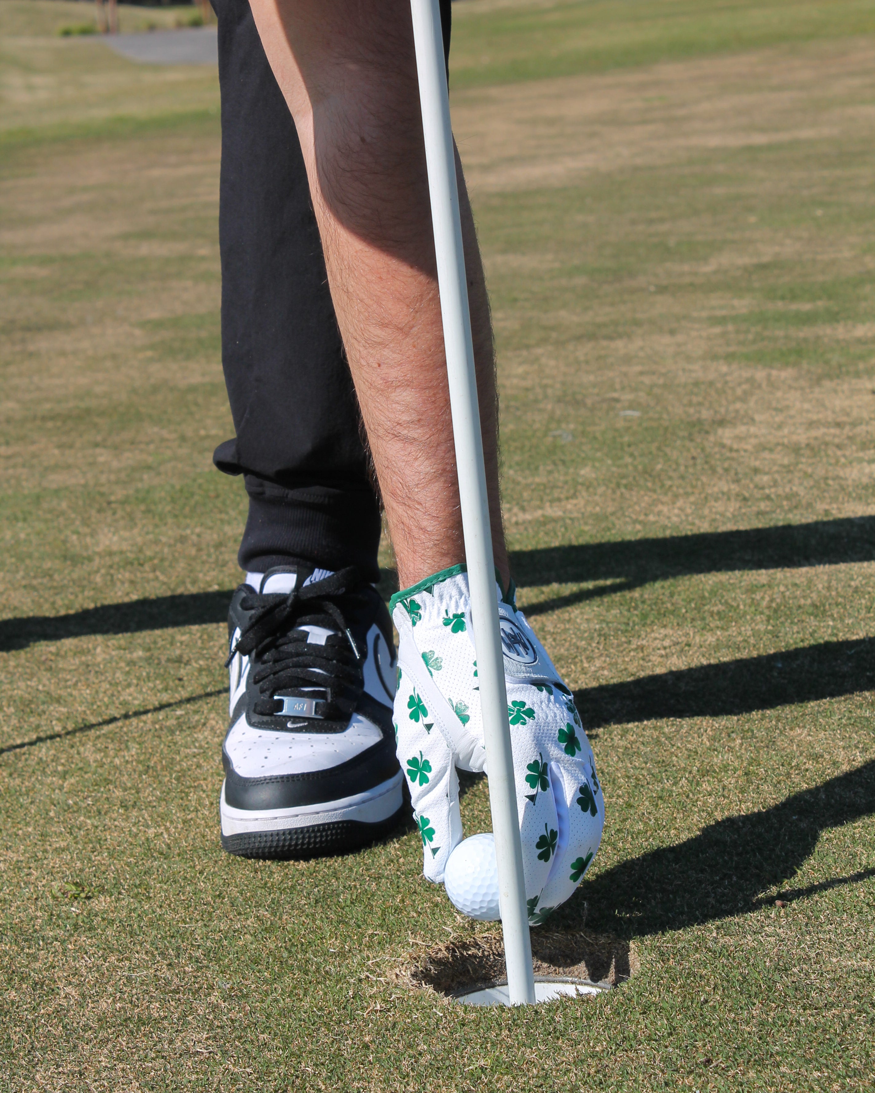 Person preparing to putt and he is removing the golf ball from the hole in a premium 'Clover Luck' golf glove
