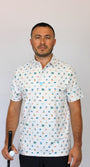 A man wearing a white short-sleeve button-up shirt with a colorful golf-themed and beach-theme, Myrtle Beach, SC pattern, holding a golf club and ball.
