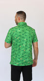 A man viewed from behind wearing a camo green short-sleeve button-up shirt with alligators on a golf coarse print in dark green, paired with black shorts, against a plain white background.