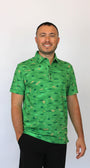 A man wearing a green short-sleeve polo shirt with an all-over camouflage pattern and Alligators on a golf course some with sunglasses, some with a golf ball in their mouth, paired with black pants, standing against a plain white background.