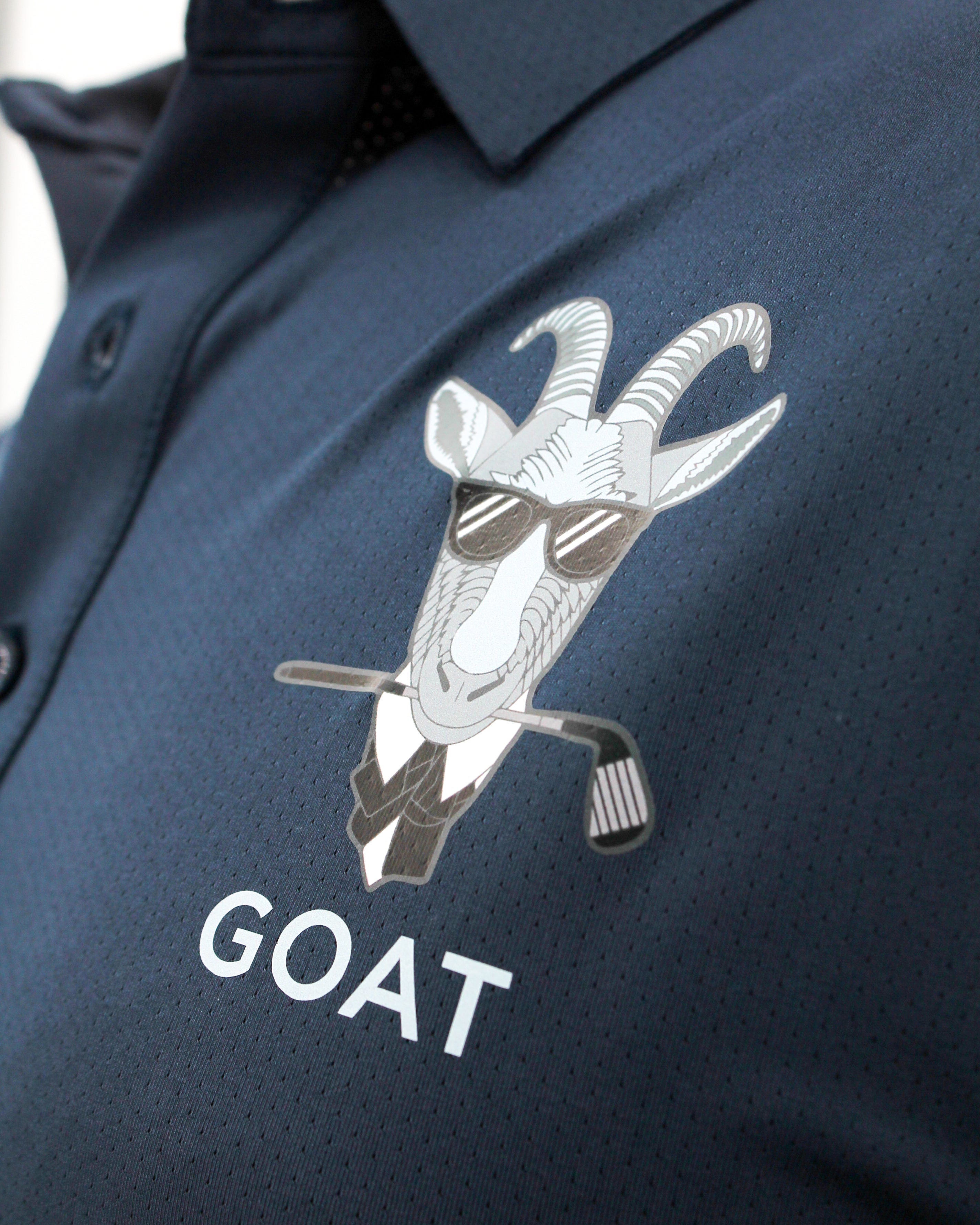 Navy blue polo shirt with a goat graphic and 'GOAT' text on a blurred background