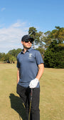 Man on a golf course wearing the Goat denim polo shirt, black pants, and sunglasses.