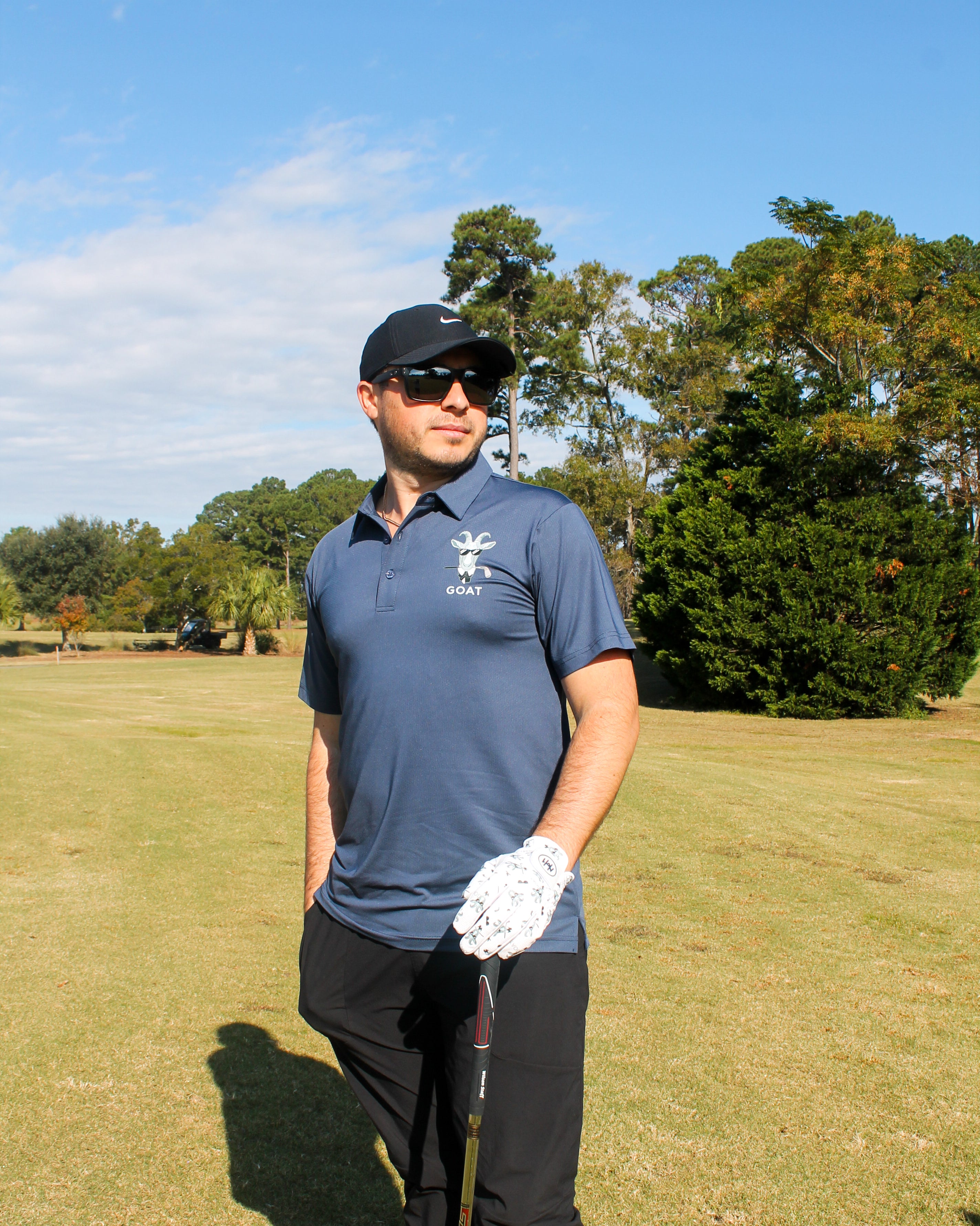 Man on a golf course wearing a blue shirt and black cap, holding a golf club.