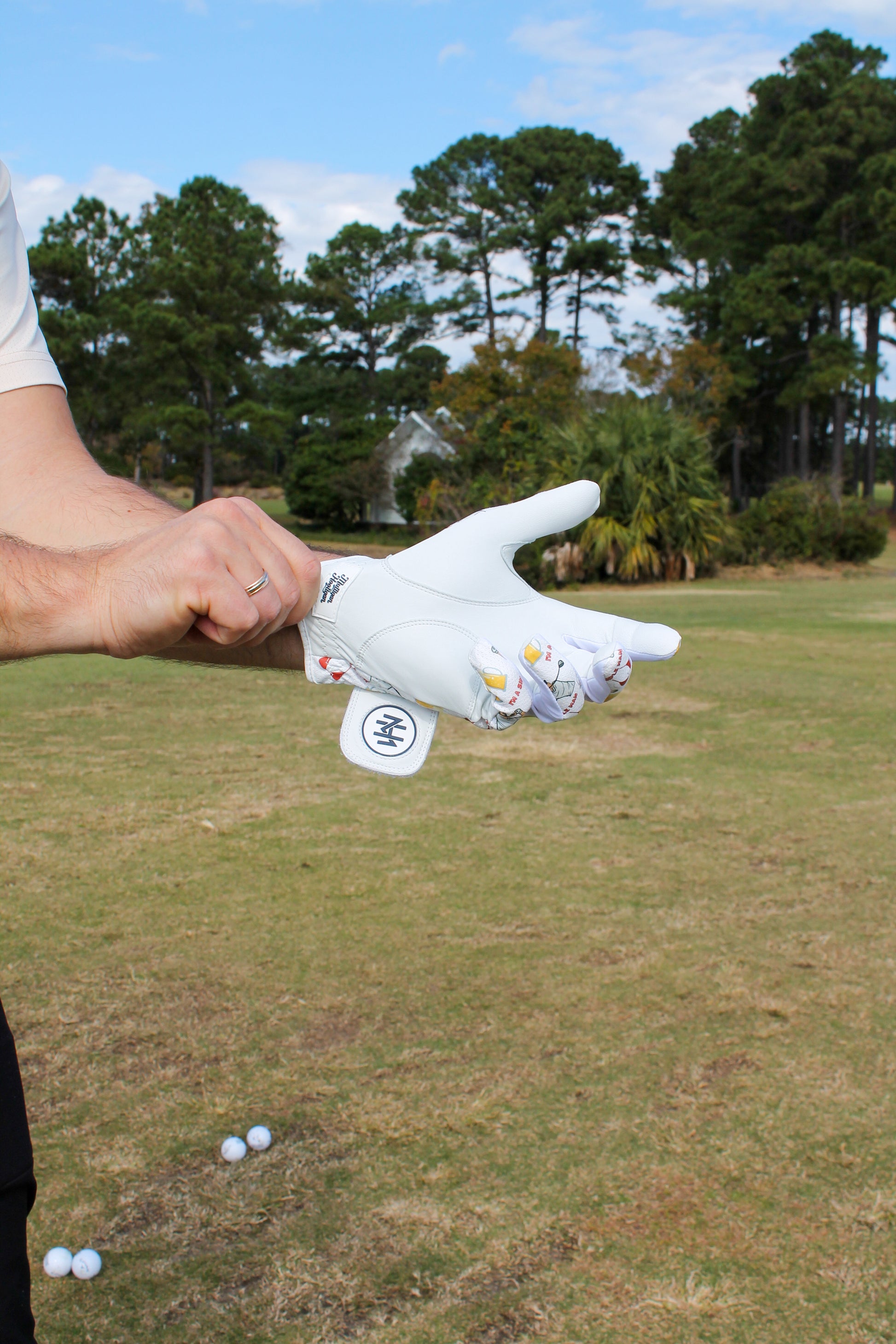 Person holding the 'I'm a simple man' golf glove on a golf course with trees in the background