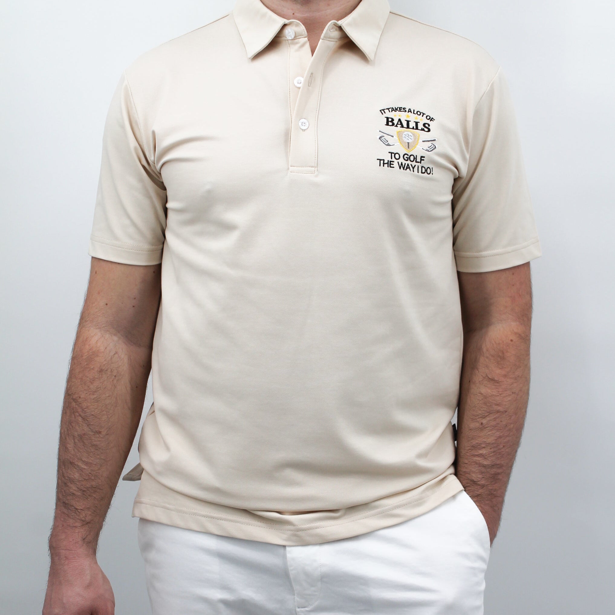 A man wearing a beige polo shirt with the chest artwork: 'It takes a Lot of Balls to play the way I do' with short sleeves, standing against a plain background.