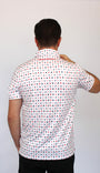 A man viewed from behind wearing a white short-sleeve button-up shirt with playing cards repeating pattern of small red and blue geometric shapes, paired with black pants, against a plain light gray background.