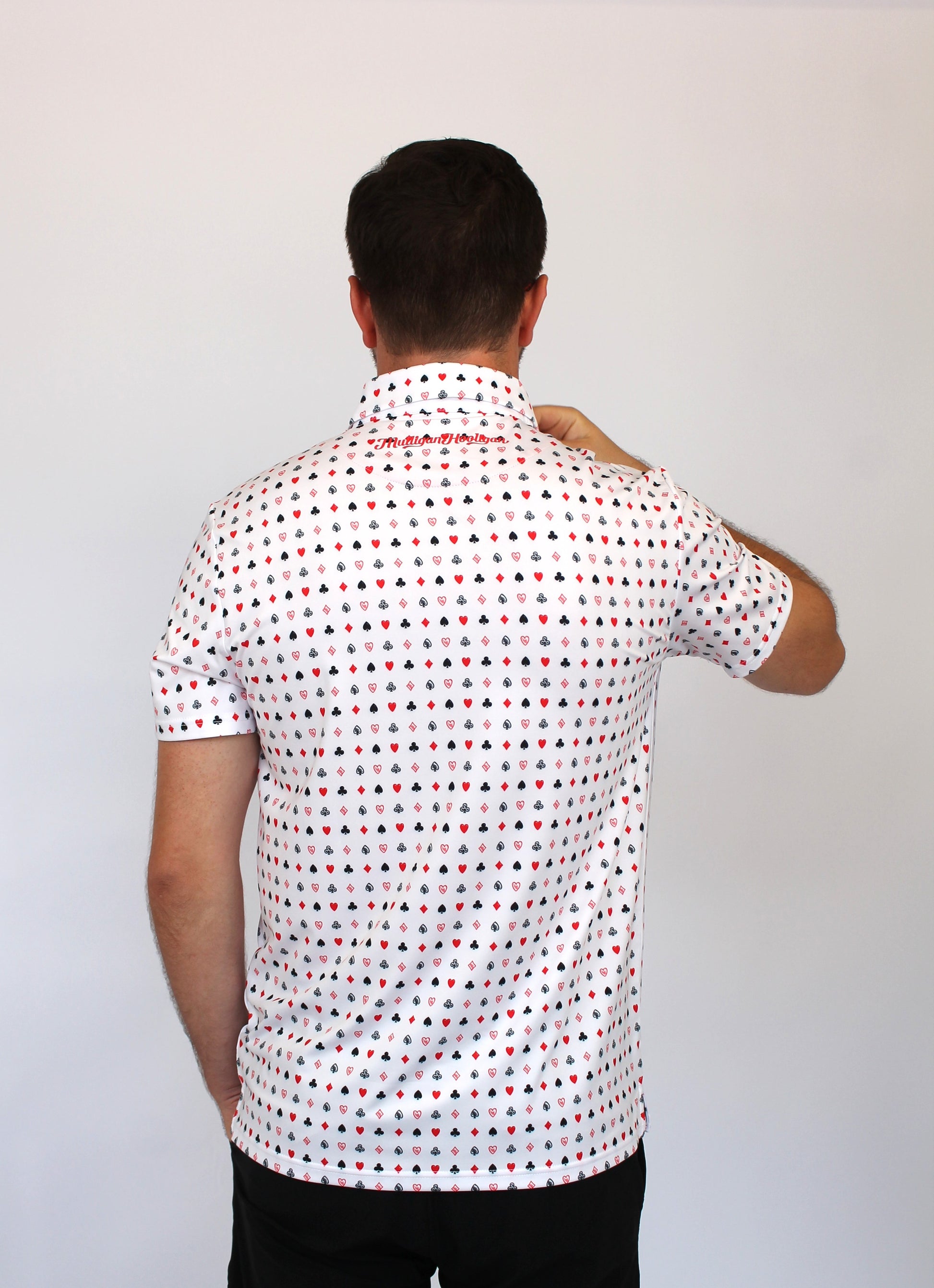 A man viewed from behind wearing a white short-sleeve button-up shirt with playing cards repeating pattern of small red and blue geometric shapes, paired with black pants, against a plain light gray background.