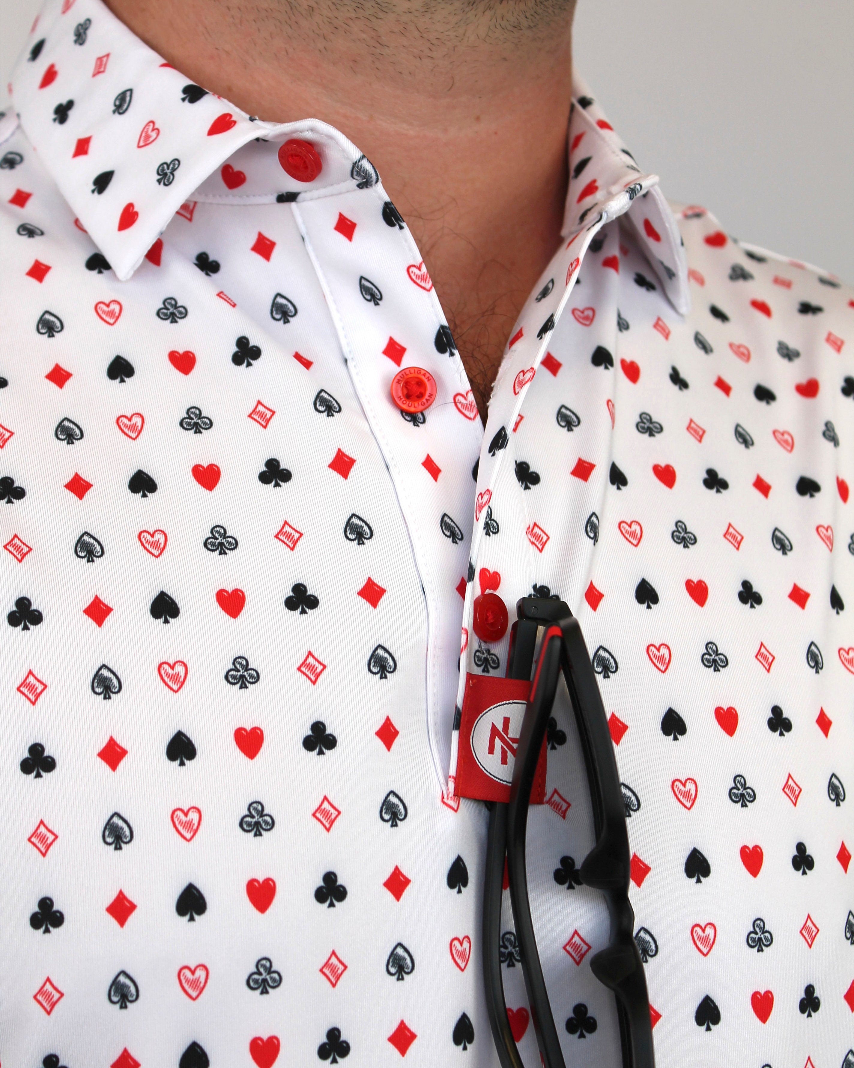 A close-up of a man wearing a white button-down shirt with a repeating playing cards pattern of red, black, and gray playing card suits.