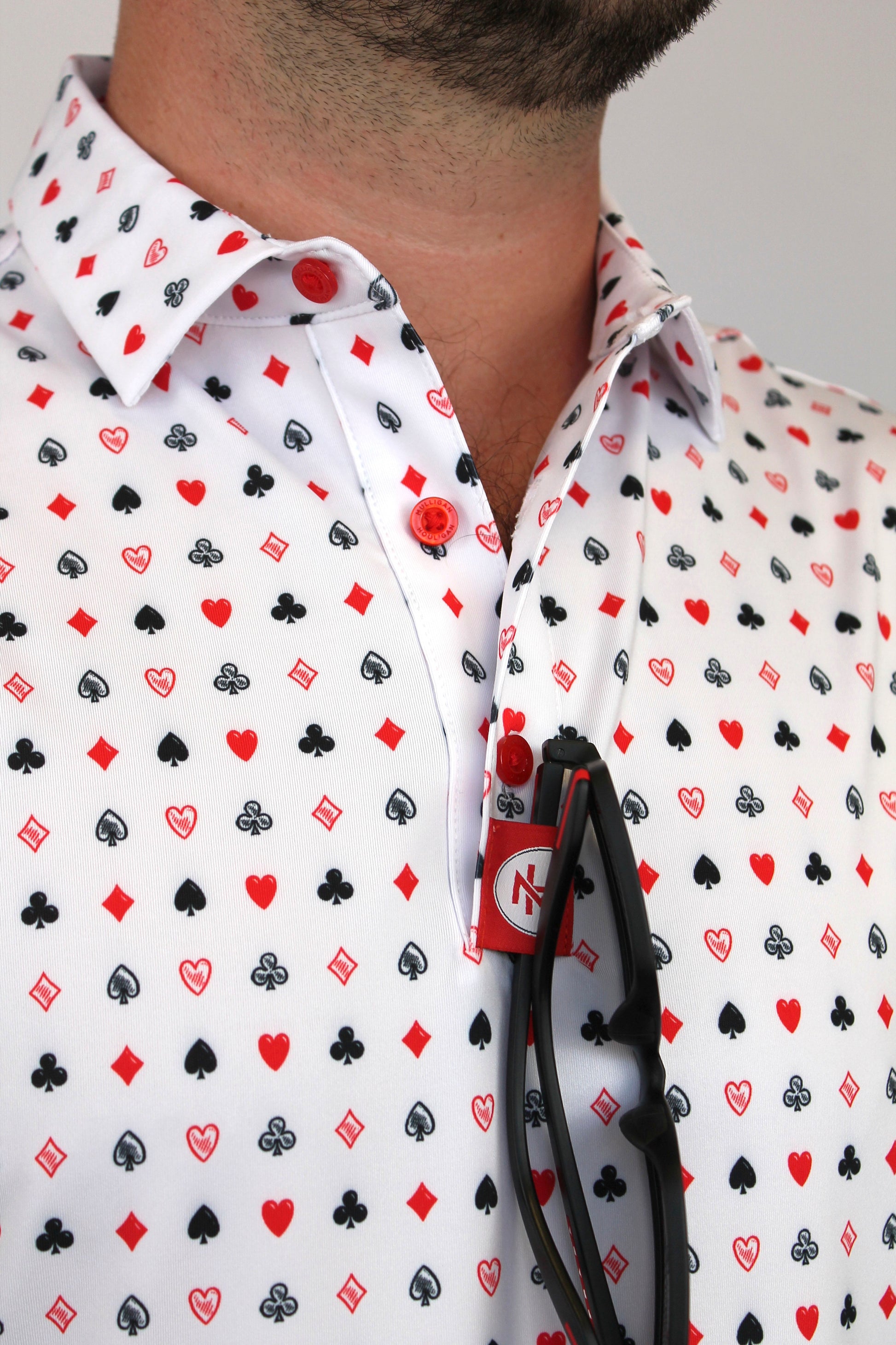 A close-up of a man wearing a white button-down shirt with a repeating playing cards pattern of red, black, and gray playing card suits.