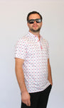 A man wearing a white short-sleeve polo shirt with a small red and blue Playing cards pattern, black pants, and dark sunglasses, standing against a light gray background.