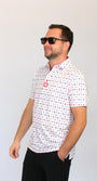 A man wearing a white short-sleeve polo shirt with a red and black playing cards pattern, black pants, and black sunglasses, standing against a plain light gray background.